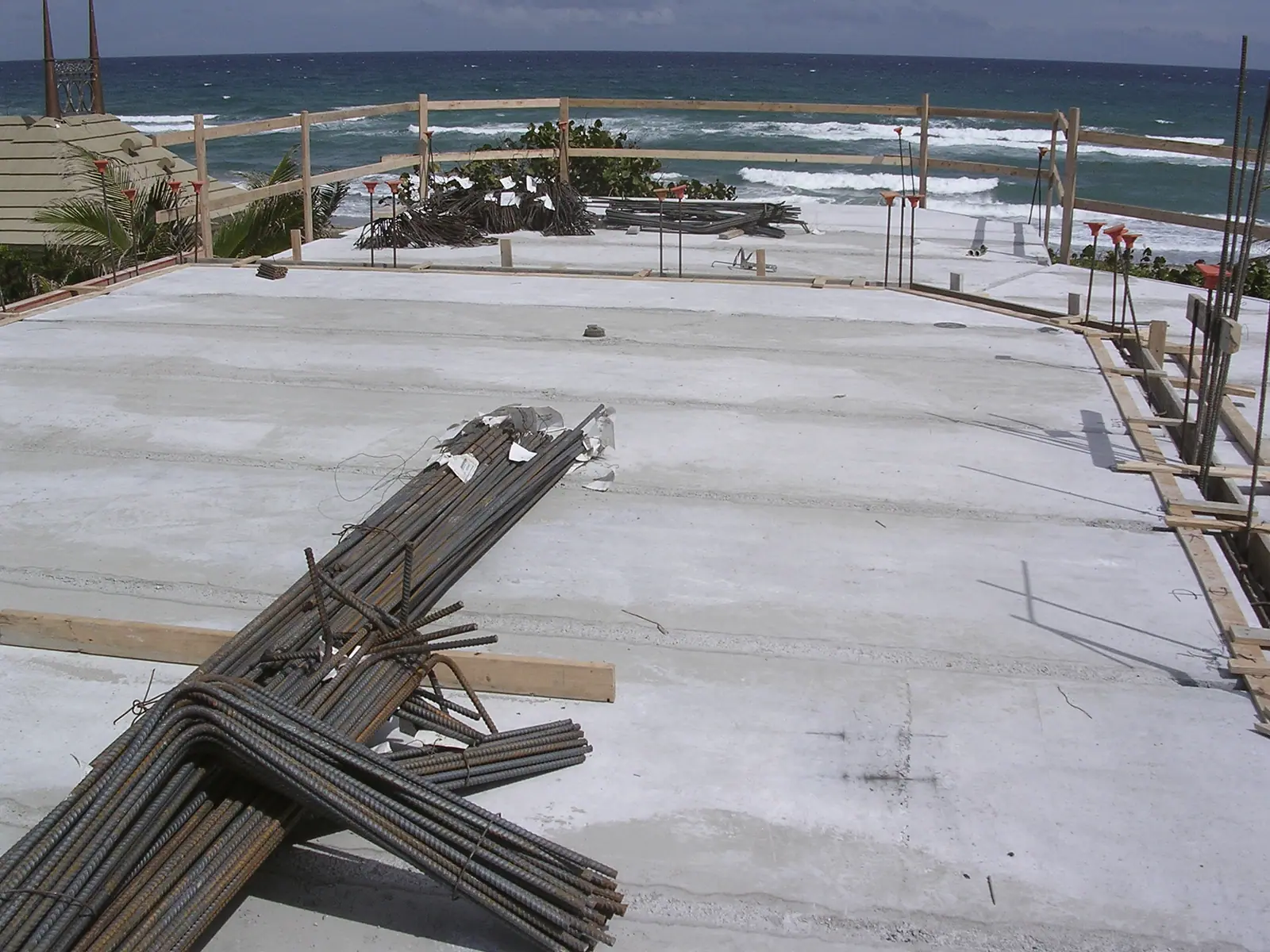 Concrete deck with bundles of rebar and wood guardrails overlooking ocean surf